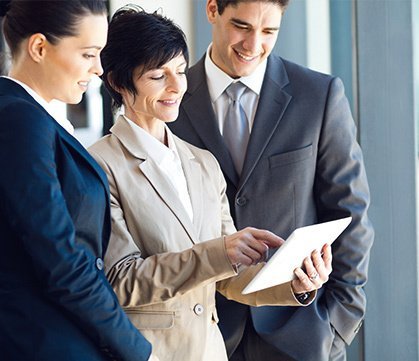 Three businesspeople looking at a tablet together, smiling. Beige and blue suits.