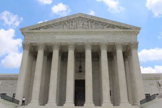 Front view of the U.S. Supreme Court building with tall columns, under a blue sky with clouds.